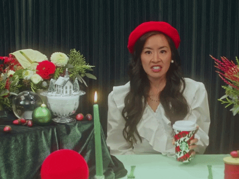 female-presenting person with a red beret on, holding a christmas-themed coffee cup, yelling "Holidays are Here!"