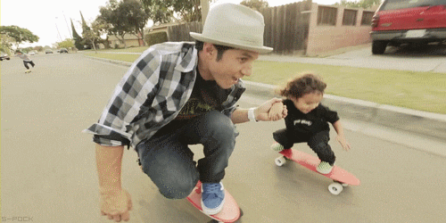 gif of a man on a skateboard coasting and holding hands with a little kid next to him on a smaller board
