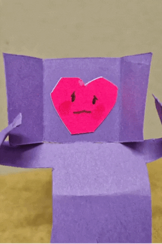 gif of a purple paper figure with a sad red heart on its face folding another facial expression on top to hide the sad heart